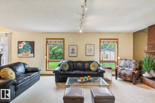 Spacious living area featuring light-colored carpet flooring, recessed track lighting, and a brick-faced fireplace with a hearth - 15804 80 Street, Edmonton, AB 