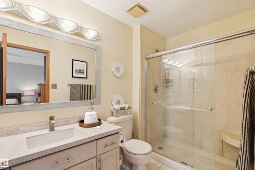 Full primary-bathroom featuring a single vanity with an integrated sink, a large mirror with a textured frame, a toilet, and a glass-enclosed shower with a built-in bench - 15804 80 Street, Edmonton, AB 