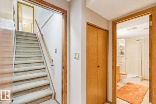Carpeted staircase with wood handrail, featuring a nearby bathroom with a glass-enclosed shower, tiled walls, and ceramic tile flooring - 15804 80 Street, Edmonton, AB 