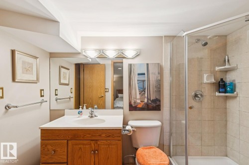 Bathroom featuring a wood-finish vanity with an integrated sink, a glass-enclosed shower with tiled walls, and a chrome light fixture - 15804 80 Street, Edmonton, AB 