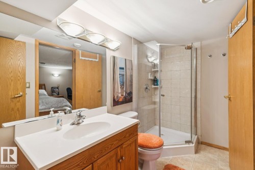 Bathroom featuring a wood-finish vanity with a white countertop and integrated sink, a glass-enclosed shower with tile surround, and tile flooring - 15804 80 Street, Edmonton, AB 