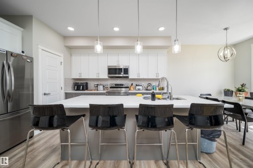 Open-concept kitchen featuring an expansive island with seating, stainless steel appliances, white cabinetry, and wood-finish flooring - 16123 31 Avenue, Edmonton, AB 