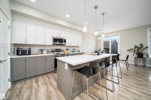 Modern kitchen featuring wood-finish flooring, two-tone cabinetry with white upper and gray lower cabinets, stainless steel appliances, a gray tiled backsplash, and recessed and pendant lighting fixtures - 16123 31 Avenue, Edmonton, AB 