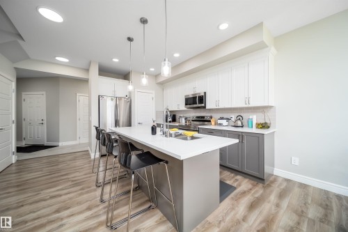 Modern kitchen featuring a large island with seating, stainless steel appliances, a white tile backsplash, light wood-finish flooring, and recessed ceiling lighting - 16123 31 Avenue, Edmonton, AB 