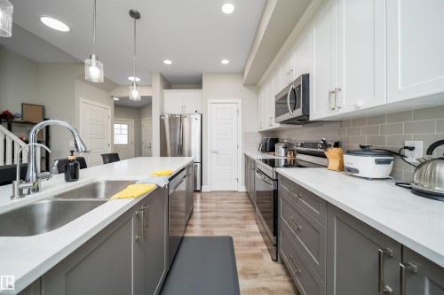 Modern kitchen featuring two-tone cabinetry, stainless steel appliances, a subway tile backsplash, and wood-finish flooring - 16123 31 Avenue, Edmonton, AB 