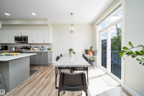 Open-concept kitchen and dining area featuring wood-finish flooring, two-tone cabinetry with stainless steel hardware, and a center island with a light-colored countertop - 16123 31 Avenue, Edmonton, AB 