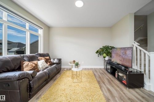 Spacious living area featuring expansive windows, wood-finish flooring, a white-painted staircase with white railings, recessed ceiling lighting, and light-toned wall finishes - 16123 31 Avenue, Edmonton, AB 