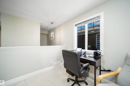 Carpeted loft area featuring a large window with blinds, a half-wall partition, and a contemporary ceiling light fixture - 16123 31 Avenue, Edmonton, AB 