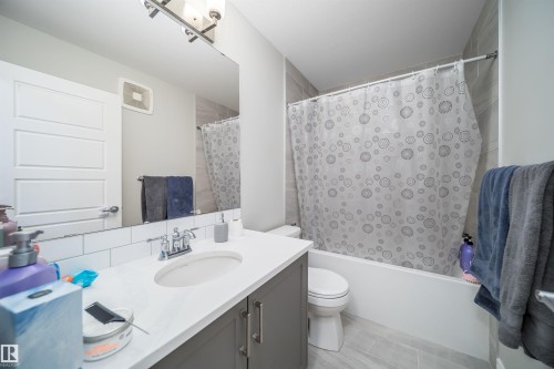 Bathroom featuring a white subway tile backsplash, a vanity with gray cabinetry and a white countertop, a shower-over-tub combination with light-colored wall tiling, and light tile flooring - 16123 31 Avenue, Edmonton, AB 