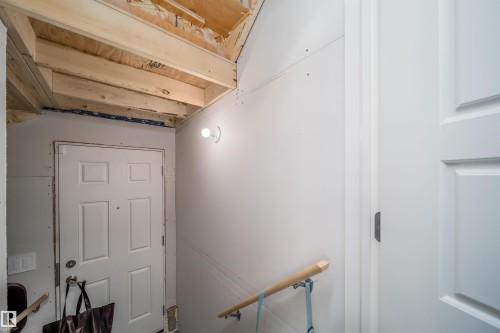 Unfinished entryway featuring exposed ceiling joists and plywood subfloor, a white paneled door, a wall-mounted light fixture, and drywall-finished walls - 16123 31 Avenue, Edmonton, AB 