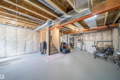 Unfinished basement featuring exposed wood joists, structural beams, insulation, and a water heater - 16123 31 Avenue, Edmonton, AB 