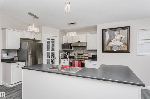 Modern kitchen featuring white cabinetry, stainless steel appliances, a multi-tone tile backsplash, and a large central island with an undermount sink - 4228 162 Avenue, Edmonton, AB 