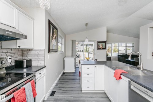 Kitchen featuring white cabinetry, dark countertops, wood-finish flooring, a stainless steel range hood, and a dual-basin sink with a gooseneck faucet - 4228 162 Avenue, Edmonton, AB 