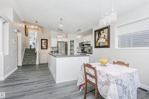 Open-concept kitchen and dining area featuring light gray wood-finish flooring, white cabinetry, a kitchen island with a gray countertop, stainless steel appliances, and a vaulted ceiling - 4228 162 Avenue, Edmonton, AB 