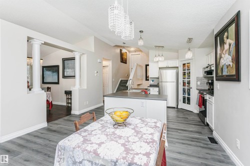 Open-concept kitchen and dining area featuring wood-finish flooring, white cabinetry, a kitchen island with sink, stainless steel appliances, and crystal-style pendant lighting - 4228 162 Avenue, Edmonton, AB 