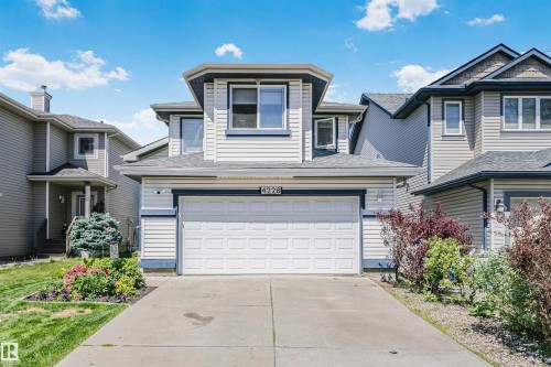 Two-story residence featuring light-colored siding with dark trim accents, an attached two-car garage, concrete driveway, and mature landscaping - 4228 162 Avenue, Edmonton, AB 