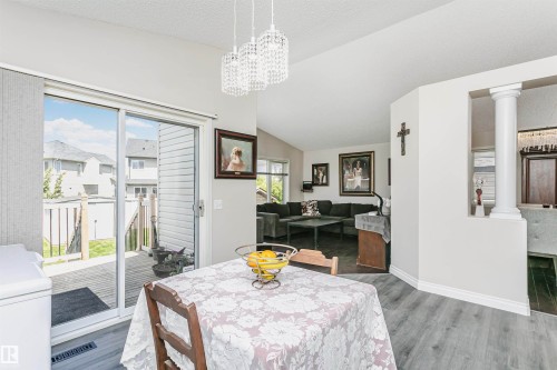 Dining area featuring wood-finish flooring, a sliding glass door to an exterior deck, and overhead crystal chandeliers - 4228 162 Avenue, Edmonton, AB 