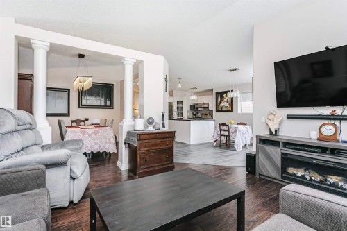 Open-concept living area featuring rich wood-finish flooring, a built-in media console with an electric fireplace, and an architectural archway with decorative columns - 4228 162 Avenue, Edmonton, AB 