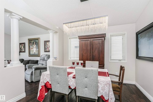 Dining area featuring a linear crystal chandelier, two windows with blinds, and dark wood-finish flooring - 4228 162 Avenue, Edmonton, AB 