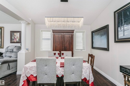 Dining area featuring wood-finish flooring, a rectangular crystal chandelier, a dark wood built-in cabinet, and white window blinds - 4228 162 Avenue, Edmonton, AB 