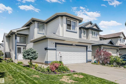 Two-story residential property featuring light-colored siding with dark trim accents, an attached garage, a concrete driveway, and landscaped front yard with shrubs and a small tree - 4228 162 Avenue, Edmonton, AB 