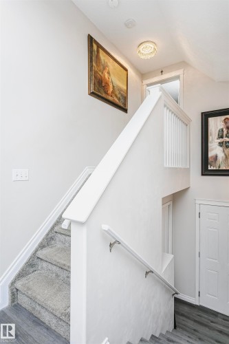 Staircase featuring light gray carpeted treads, white painted risers, and a white balustrade - 4228 162 Avenue, Edmonton, AB 