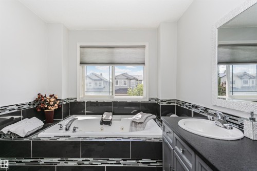Soaking tub featuring a tiled surround with mosaic accents, a chrome faucet, and a window with a cellular shade - 4228 162 Avenue, Edmonton, AB 