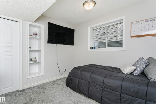 Room featuring light gray wall paint, textured ceiling, a built-in shelving unit, white baseboards, and gray carpet flooring - 4228 162 Avenue, Edmonton, AB 