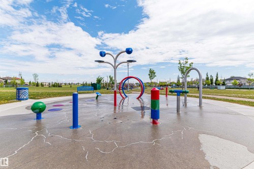 Splash pad featuring multiple colorful water play structures, a textured concrete surface, and surrounding green space with mature trees - 4228 162 Avenue, Edmonton, AB 