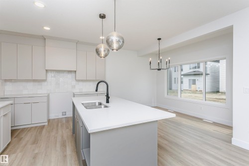 Contemporary kitchen featuring light gray cabinetry, white tile backsplash, a center island with an undermount sink and matte black faucet, and wood-finish flooring - 6210 Dansereau Crescent, Beaumont, AB 