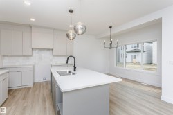 Contemporary kitchen featuring light gray cabinetry, white tile backsplash, a center island with an undermount sink and matte black faucet, and wood-finish flooring - 