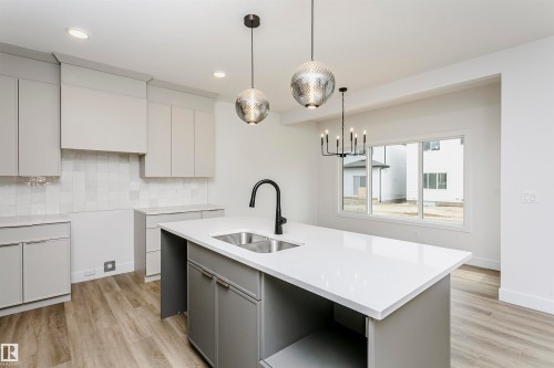 Modern kitchen featuring a central island with dual sinks, light gray cabinetry, quartz countertops, and wood-finish flooring - 6210 Dansereau Crescent, Beaumont, AB 