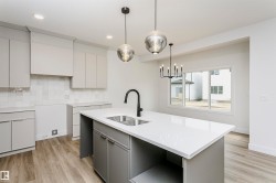 Modern kitchen featuring a central island with dual sinks, light gray cabinetry, quartz countertops, and wood-finish flooring - 
