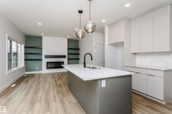 Open-concept living space with a modern kitchen island, wood-finish flooring, and built-in shelving surrounding an electric fireplace - 