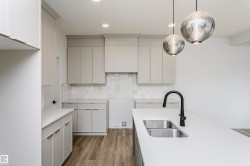 Kitchen featuring an island with a dual basin sink and matte black faucet, light grey cabinetry, tile backsplash, and wood-finish flooring - 