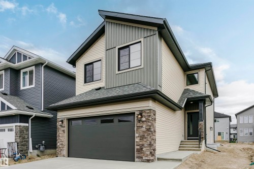 Contemporary multi-story residence featuring light beige and gray siding, a dark gray garage door, and stone facade accents - 6210 Dansereau Crescent, Beaumont, AB 