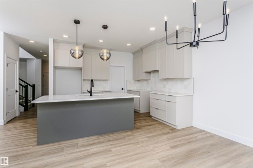 Open-concept kitchen featuring a large island with a sink and modern faucet, light grey cabinetry, white countertops, and a white subway tile backsplash - 6210 Dansereau Crescent, Beaumont, AB 