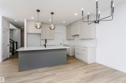 Open-concept kitchen featuring a large island with a sink and modern faucet, light grey cabinetry, white countertops, and a white subway tile backsplash - 