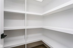 Expansive pantry featuring built-in white shelving, wood-finish flooring, and a black lever door handle - 