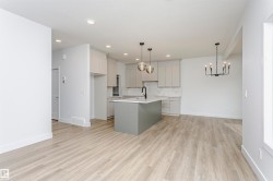 Contemporary kitchen featuring a center island with a black faucet, light gray cabinetry, and a subway tile backsplash - 