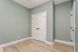 Interior room featuring light green walls, wood-finish flooring, white baseboards, and white two-panel doors with matte black hardware - 