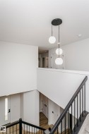 Modern tiered pendant lighting illuminates the open interior featuring a black metal and wood-finish staircase railing, white panel doors with black hardware, and wood-finish flooring - 