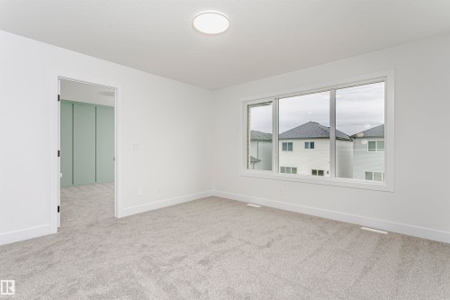 Bright interior space featuring a large three-panel window, light gray carpeting, and a flush-mount ceiling light fixture - 6210 Dansereau Crescent, Beaumont, AB 