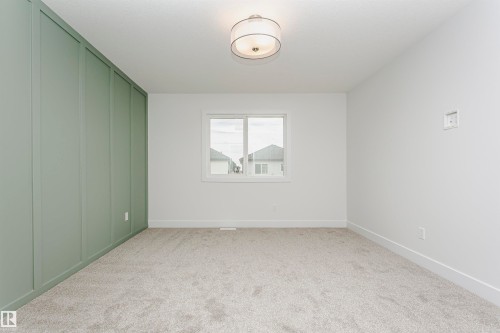 Room featuring a light green accent wall with vertical paneling, white walls, and light gray carpeted flooring - 6210 Dansereau Crescent, Beaumont, AB 