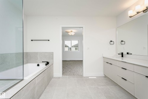 Spacious bathroom featuring a dual vanity with a large mirror, a built-in bathtub with tiled surround, a separate glass-enclosed shower, and large format tile flooring - 6210 Dansereau Crescent, Beaumont, AB 