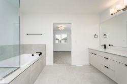 Spacious bathroom featuring a dual vanity with a large mirror, a built-in bathtub with tiled surround, a separate glass-enclosed shower, and large format tile flooring - 