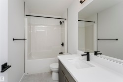 Bathroom featuring a white bathtub and shower combination, dark bronze fixtures, a rectangular vanity mirror, a single-sink vanity with a light-toned countertop, and light gray tile flooring - 