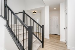 Staircase with light-toned carpeted treads, dark wood handrails, and black metal balusters - 