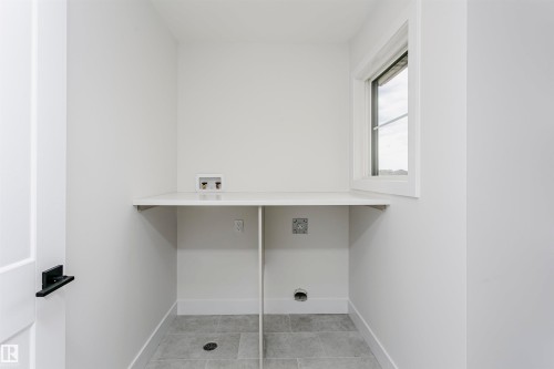 Utility room featuring a white countertop with integrated plumbing hookups, a single window, and a light gray tile floor - 6210 Dansereau Crescent, Beaumont, AB 