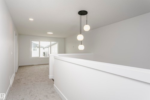 Bright upper landing featuring a contemporary three-globe pendant light, recessed lighting, white wall and trim finishes, gray carpet, and large windows - 6210 Dansereau Crescent, Beaumont, AB 